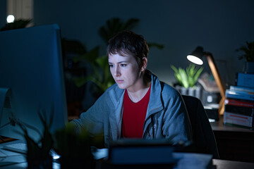 Person staring blankly at a computer screen late at night in a dark office