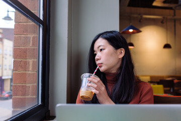 Young woman drinking iced coffee and looking through cafe window