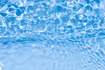 Blue water with ripples on the surface. Defocus blurred transparent blue colored clear calm water surface texture with splashes and bubbles. Water waves with shining pattern texture background.
