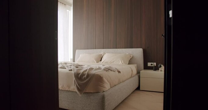 A cozy modern bedroom featuring a comfortable bed with soft bedding, wooden wall panels, and a small bedside table. Natural light filters through the window, creating a peaceful atmosphere.