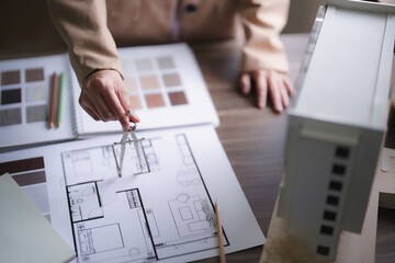 Female architect using divider compass to drawing building project and design interior on blueprint