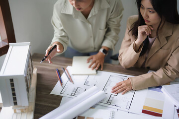 Two female architects discuss and brainstorm about building model and interior design on blueprint