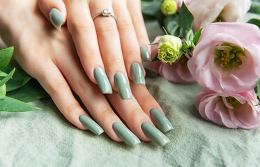 Elegant hands with green nail polish resting on a soft fabric surrounded by delicate flowers in a tranquil setting