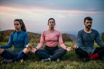 Fit sporty people practicing yoga and meditating during a late sunset period of a day outdoors