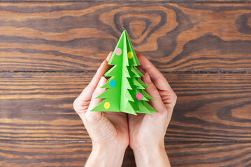Christmas tree handmade paper toy in a hands on a wooden table. Top view.