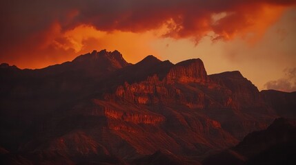 Naklejka premium Dramatic sunset over rugged mountains with vibrant orange and red hues illuminating the landscape.