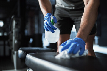 Fototapeta premium Gym, person and spray with equipment for cleaning, hygiene or health to reduce bacteria for workout. Fitness club, hands and janitor with gloves for virus safety, wipes dust or liquid soap with cloth