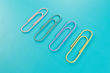 Top view of colorful paperclips on blue background. School, office wallpaper. Flat lay, copy space.