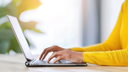 Person in yellow sweater working on laptop at sunlit desk.