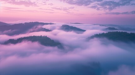 Dreamy sunrise over lush mountain range covered in dense fog and soft pink clouds