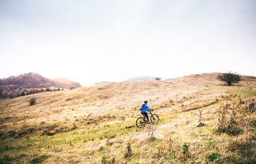 Cyclist far in the middle of beautiful nature during early autumn morning. Concept of healthy lifestyle.