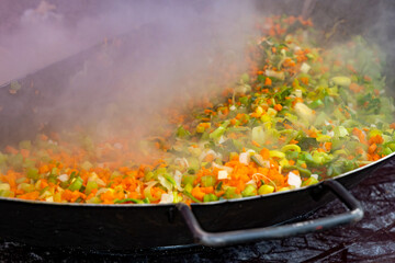Chopped carrots, leeks, and other vegetables are being cooked in a large pot with steam rising from the food