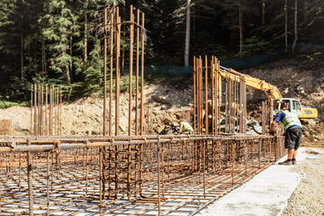 Reinforced Concrete Foundation with Rebar Rods Columns Pillars in  Construction Site in Forest. Reinforcement Construction with Excavator and Workers