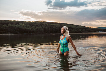 Cold water swimming for elderly women. Senior sporty women standing in lake during cold evening,...