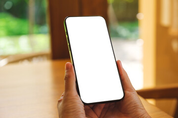 Mockup image of a woman holding and using mobile phone with blank desktop at home
