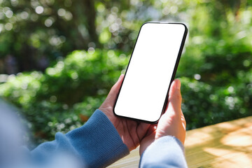 Mockup image of a woman holding mobile phone with blank white desktop screen in the outdoors