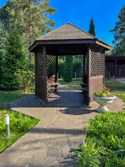 A small gazebo with a bench and a white vase with flowers in it