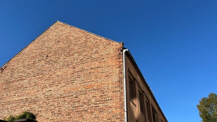 A weathered brick wall, bathed in warm sunlight, contrasting against a clear blue sky. Perfect for wallpaper, design element, or any commercial purposes.