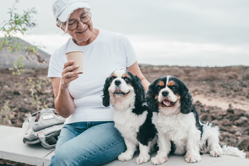 Senior smiling woman sitting outdoors with her two cavalier king charles spaniel dogs enjoying...
