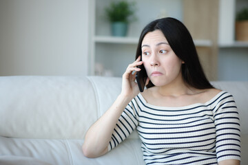 Perplexed asian woman talking on phone at home