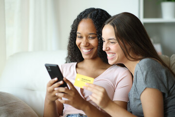 Happy interracial lesbian couple buying online with phone