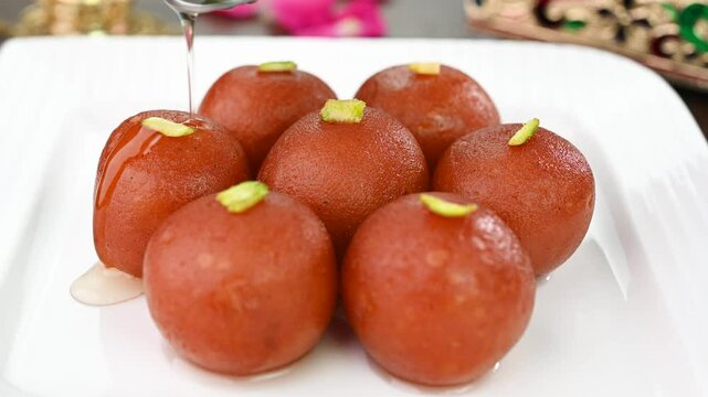 Pouring sugar syrup on gulab jamun sweet dish.