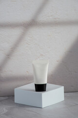 Plastic white tube for cream or lotion. Skin care or sunscreen cosmetic with stylish props on shadow window background.