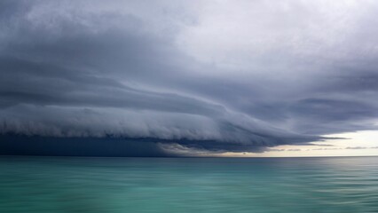 Dramatic storm clouds over calm turquoise sea.