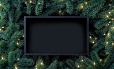une boîte noire creuse vide au milieu de branches de sapins avec guirlandes lumineuse pour présentation de produit	
