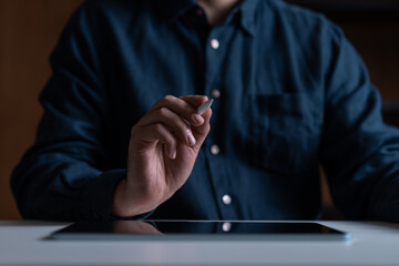 Close-up of a hand holding a stylus pen near a tablet on a table.
