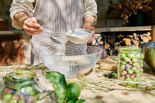 Woman adding salt in bowl of water and preparing canning brine for fermenting olives