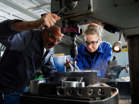 Focused trainee working with instructor near machine at workshop