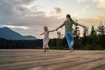 Mother and daughter holding hands and dancing together on jetty