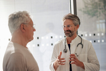 Happy senior doctor talking and explaining to man near glass