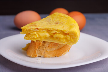 Traditional Spanish omelette skewer with bread, captured in detail with eggs in the background on a...