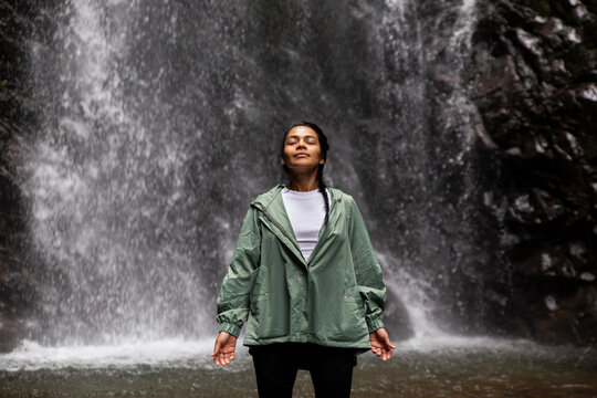 Smiling woman standing with eyes closed in front of waterfall