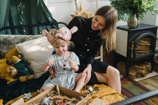 Happy mother and daughter sitting with Christmas ornaments box on bed at home