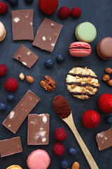 Macarons, chocolate, cookies, berries and various nuts on dark blue background. Top view.