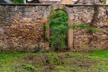A stone archway in a stone wall leads to a hidden garden area