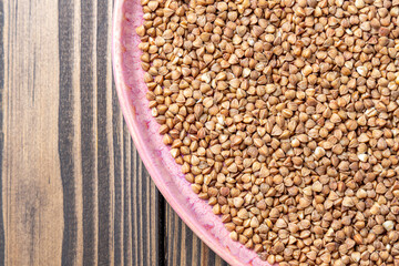 Buckwheat Grains on Plate on Wooden Background, Top View, Copy Space.Hulled kernels of buckwheat grains close up. Food background.