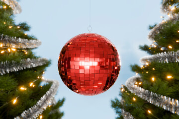 Red disco ball hanging between two decorated christmas trees