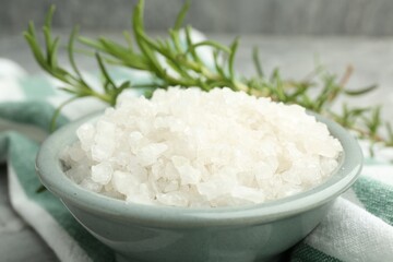 Sea salt in bowl and rosemary on table, closeup