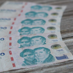 ten thousand Argentinean peso banknotes stacked in a linear fashion on a gray wooden background 
