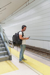 Middle-Aged Man in Casual Clothing with Backpack Using Smartphone for E-Ticket While Waiting for Train at Station