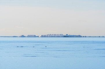 View of the Ebro Delta coast with mountains of salt from the Alfaques Bay salt flats and birds over calm blue Mediterranean waters.