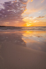 Obraz premium A beautiful pink and golden sunrise over the ocean, reflected in the sand.