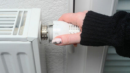 A girl turns on the heating in the apartment, hand close-up, thermostat, black sweater, manicure, white wall, heating season, home heating, Europe