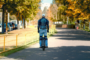 Man riding an electric unicycle in city park on bright autumn day, wearing protective gear for safety riding, eco-friendly transportation, leisure in the outdoors. EUC rider wearing protective armor