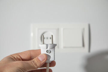Hand holding electric plug into a power outlet.