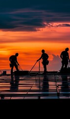 Silhouettes of workers on a rooftop at sunset.